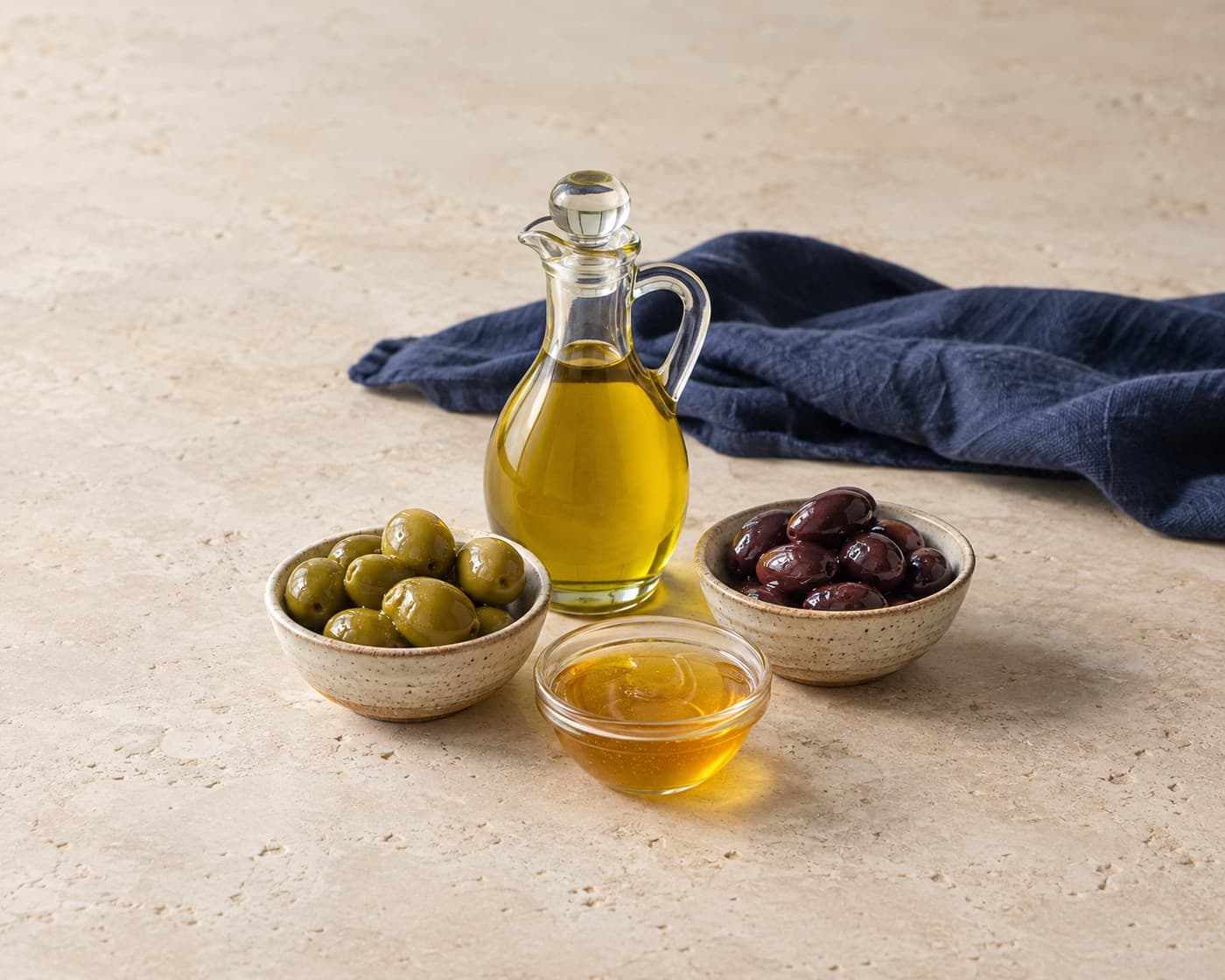 Olive oil, green and dark table olives, and raw honey on warm limestone