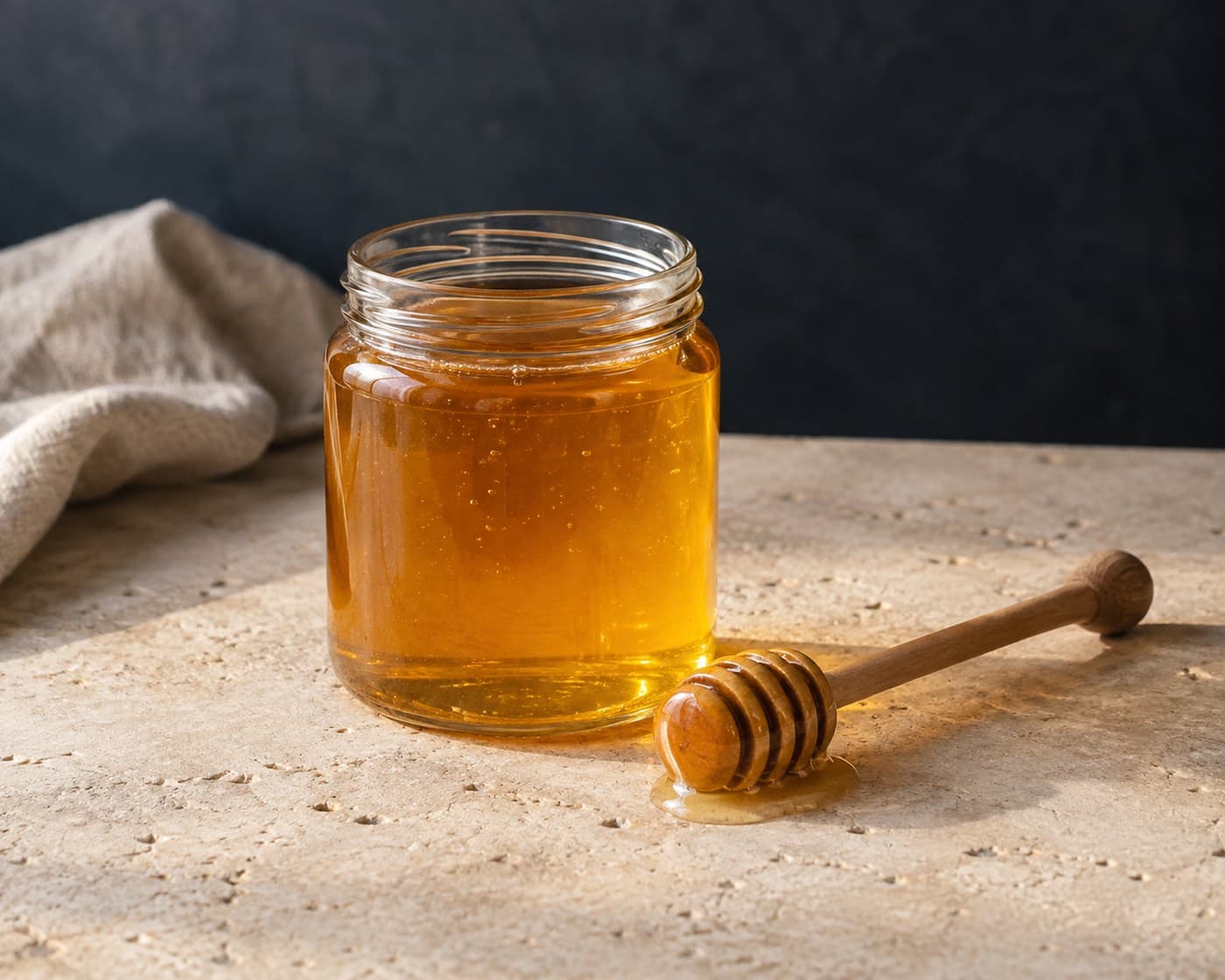 Raw honey in a clear glass jar with a wooden honey dipper